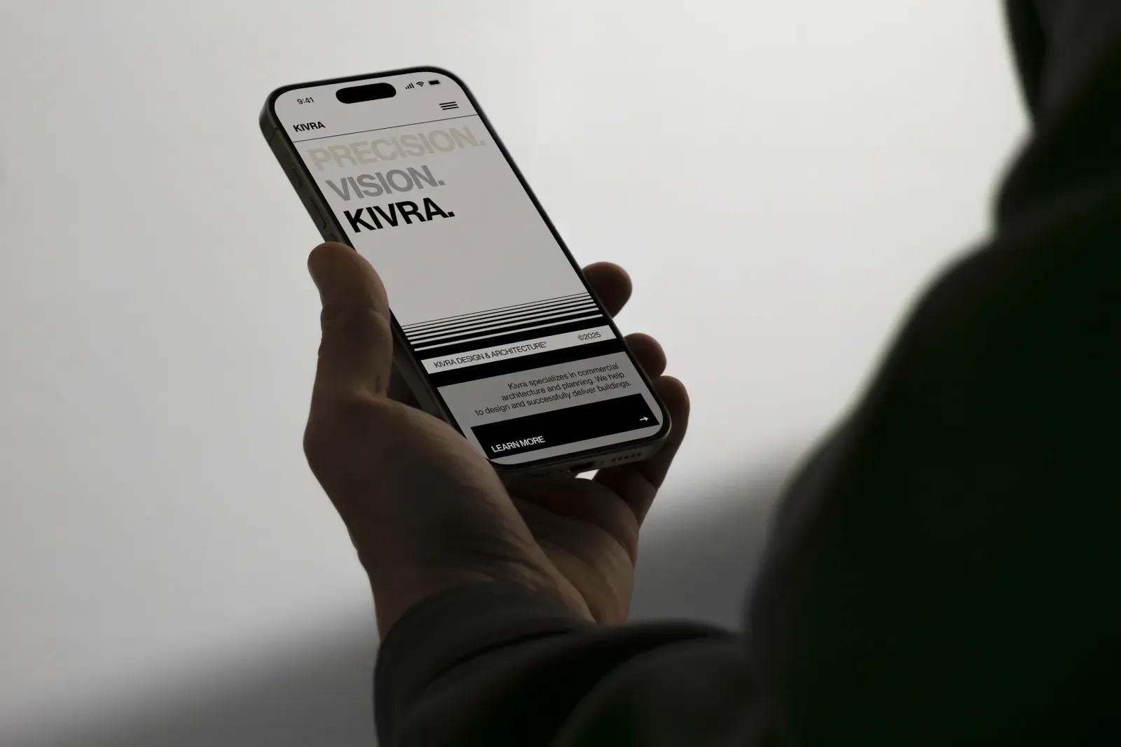 Hand holding a smartphone displaying a website with text 'PRECISION. VISION. KIVRA.' and a 'Learn More' button.