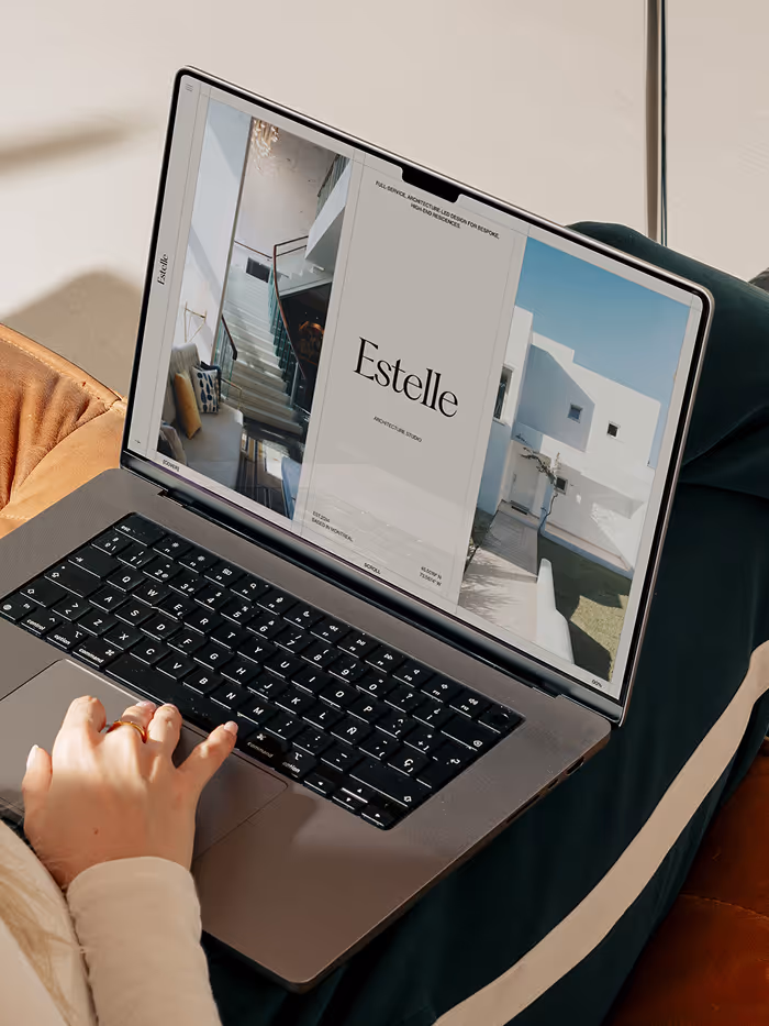 Person using a laptop showing an architectural design portfolio titled 'Estelle' with interior and exterior house photos.