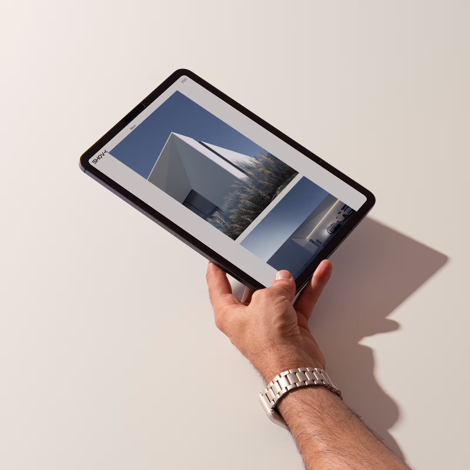 Hand holding a tablet displaying architectural photos of a modern white building against a blue sky.